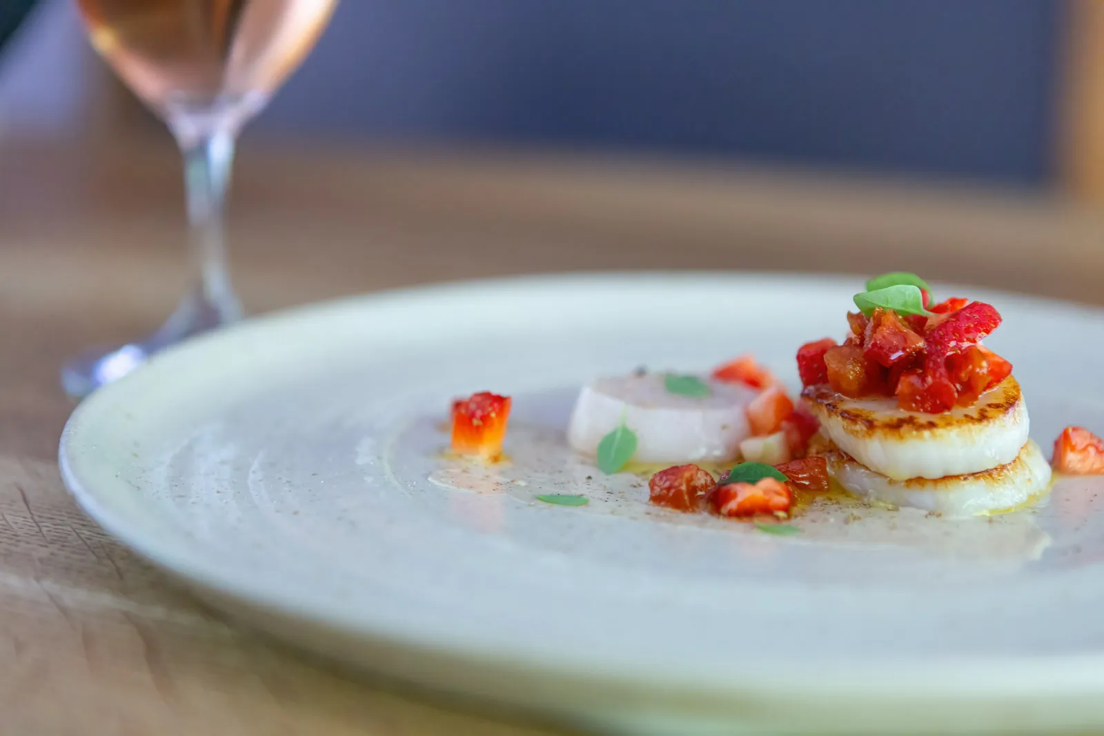 Seared scallops with vibrant red salsa and microgreens on a wide white plate at Sat Bains