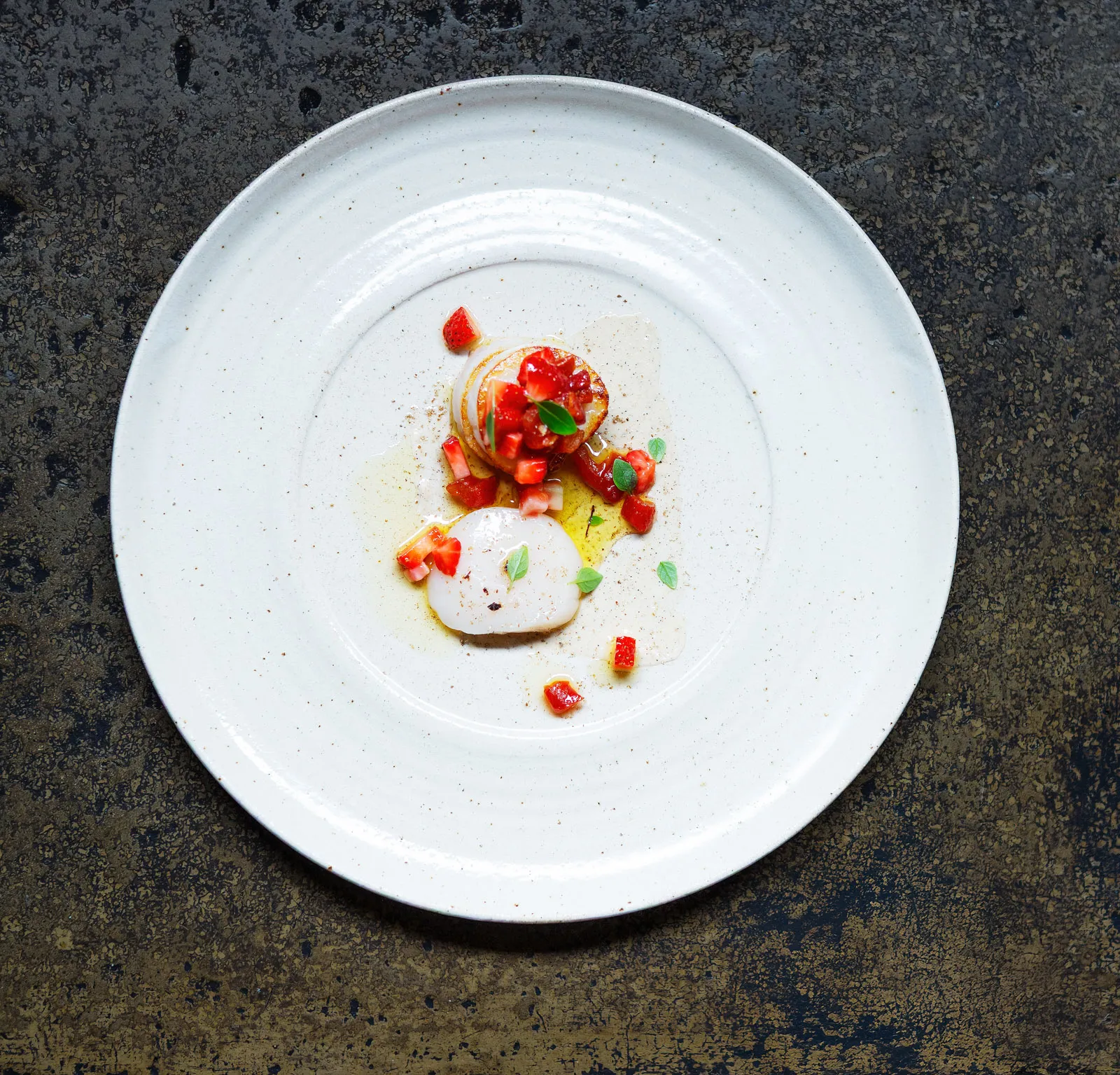 Overhead photograph of the scallop course at Sat Bains, a full circular plate on a dark rustic tabletop