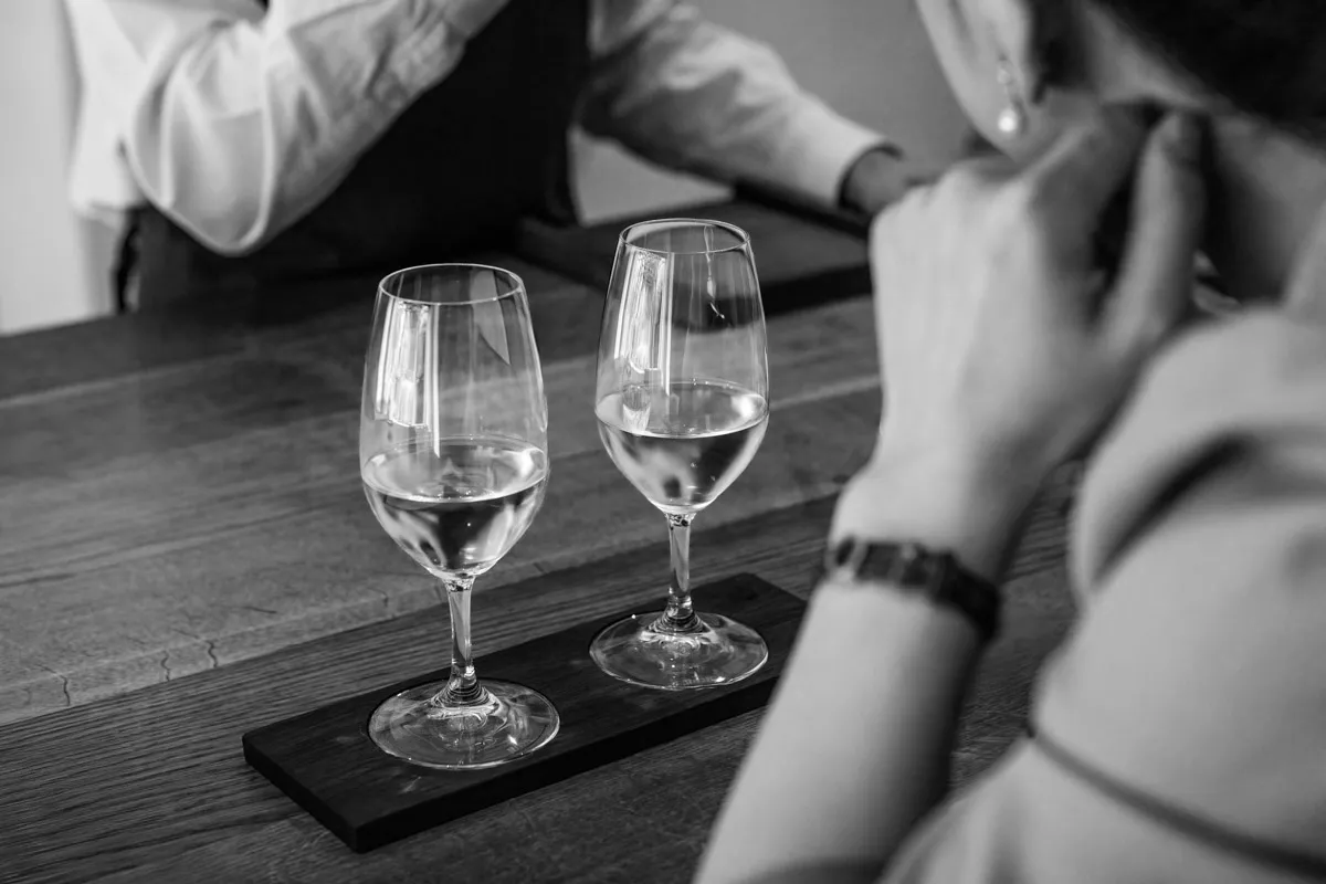 Two elegant stem glasses standing on a dark tabletop, each with a small pour of wine at Restaurant Sat Bains