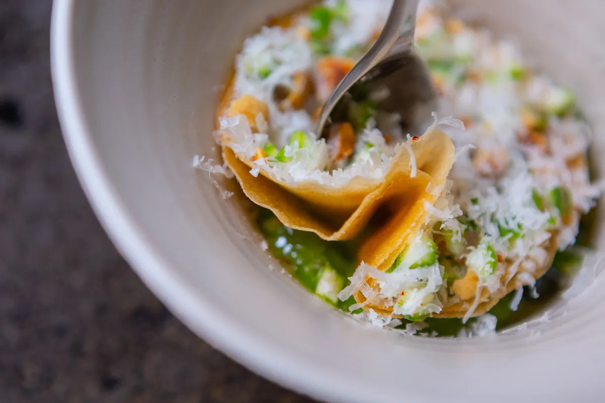 A delicate folded pastry garnished with finely grated cheese and tiny herbs, a spoon dipping into the dish at Sat Bains