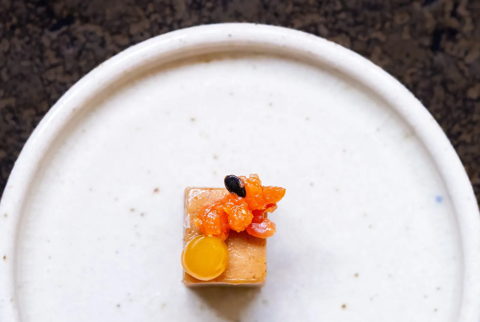 A single precise bite-sized course at Sat Bains, a cube of gelee topped with bright orange fruit compote, a yellow gel dot and a black seed